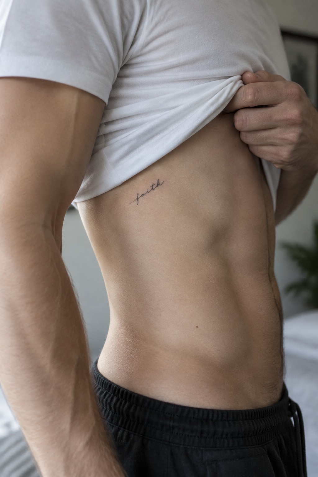 Man lifting white t-shirt to reveal faith tattoo on torso above black shorts