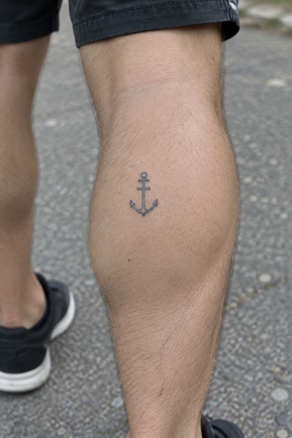 Small black anchor tattoo on the side of a man's knee