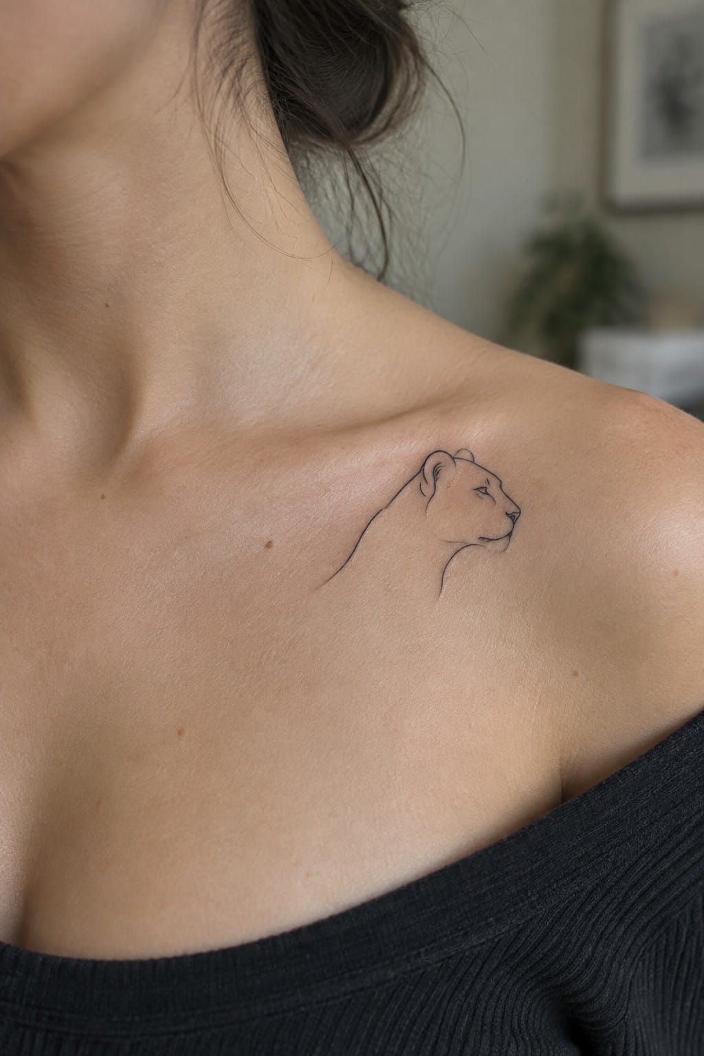 Small single-line lioness tattoo on a woman's shoulder in minimalist style.