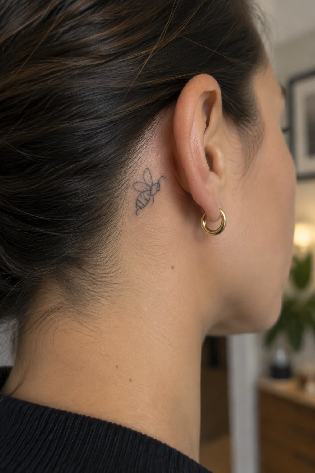 Close-up side profile showing a bee tattoo behind the ear with a gold hoop earring.