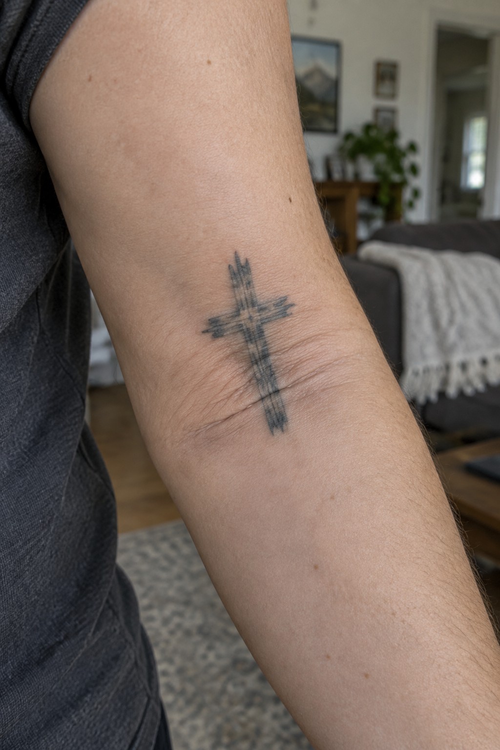 Gray sleeveless shirt reveals wooden cross tattoo on upper arm.