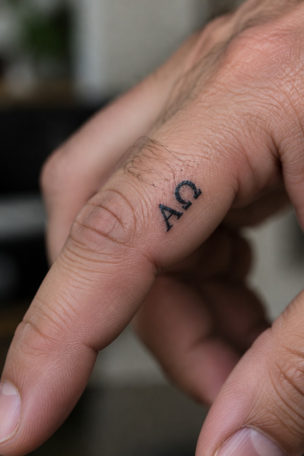 Close-up of finger with black AΩ tattoo, showing skin texture and fine hairs.