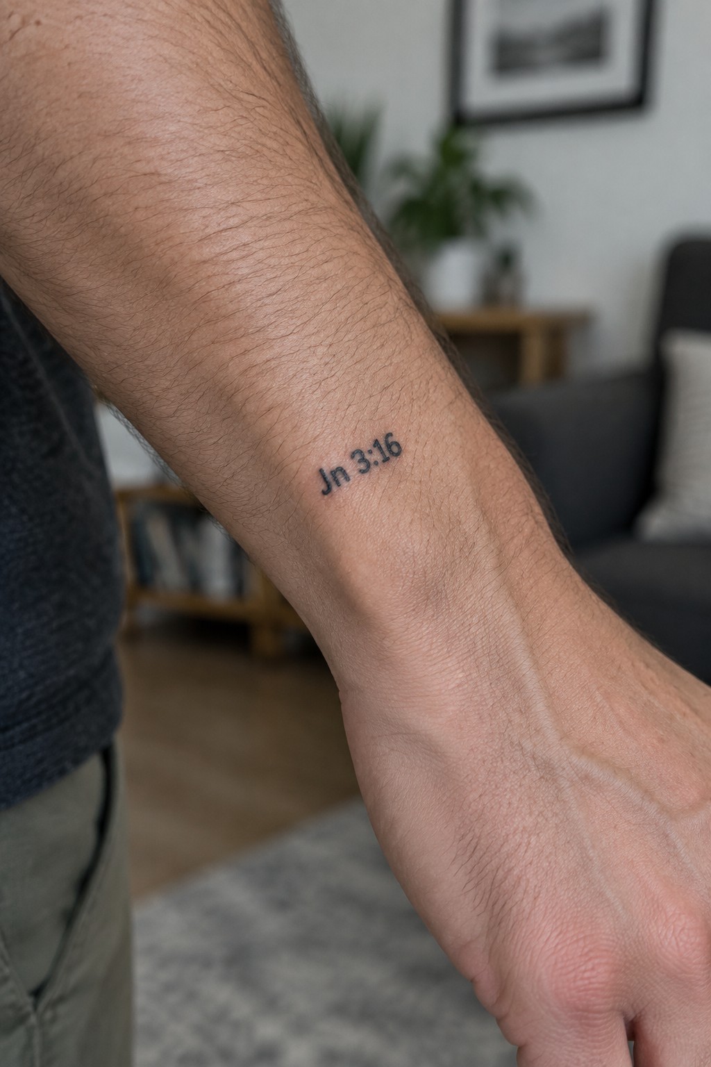 Small black text tattoo of Jn 3:16 on the inner forearm of a man