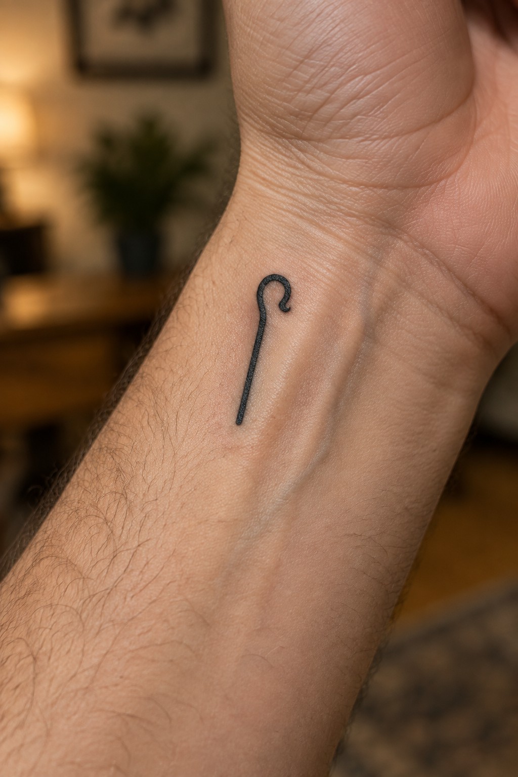 Tiny black shepherd's crook tattoo on hairy inner wrist skin