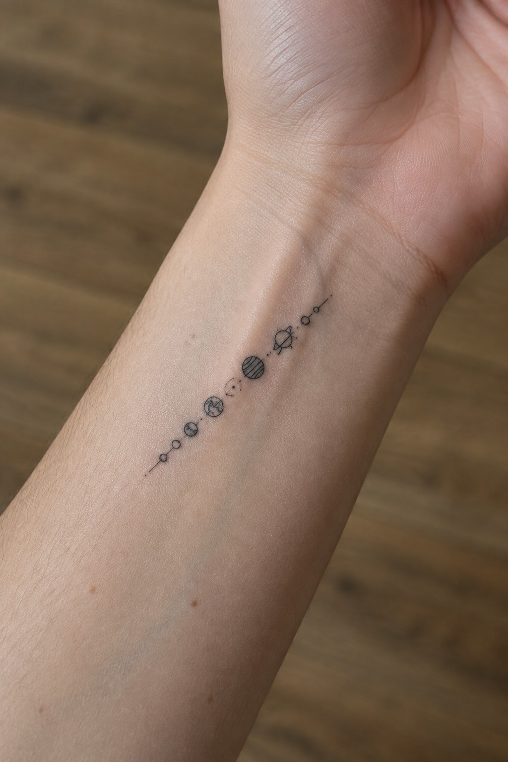 Fine line solar system tattoo in a straight line across the inner wrist