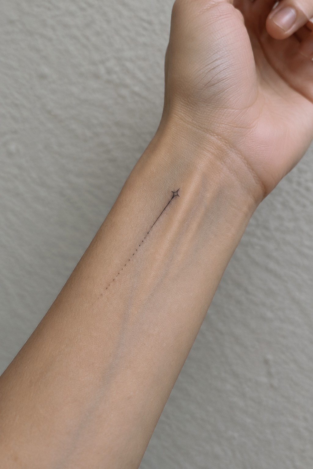 Minimalist single needle tattoo of a shooting star on the inner wrist with a dotted line turning solid and ending at a small star.
