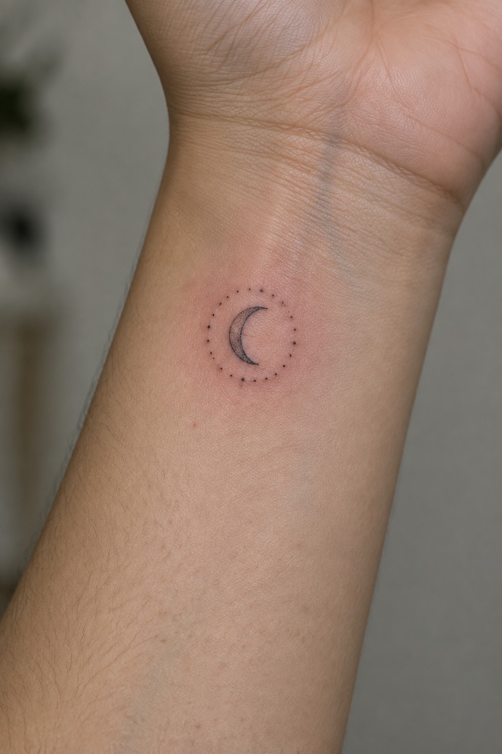 Crescent moon tattoo with dotted circle on slightly reddened wrist skin