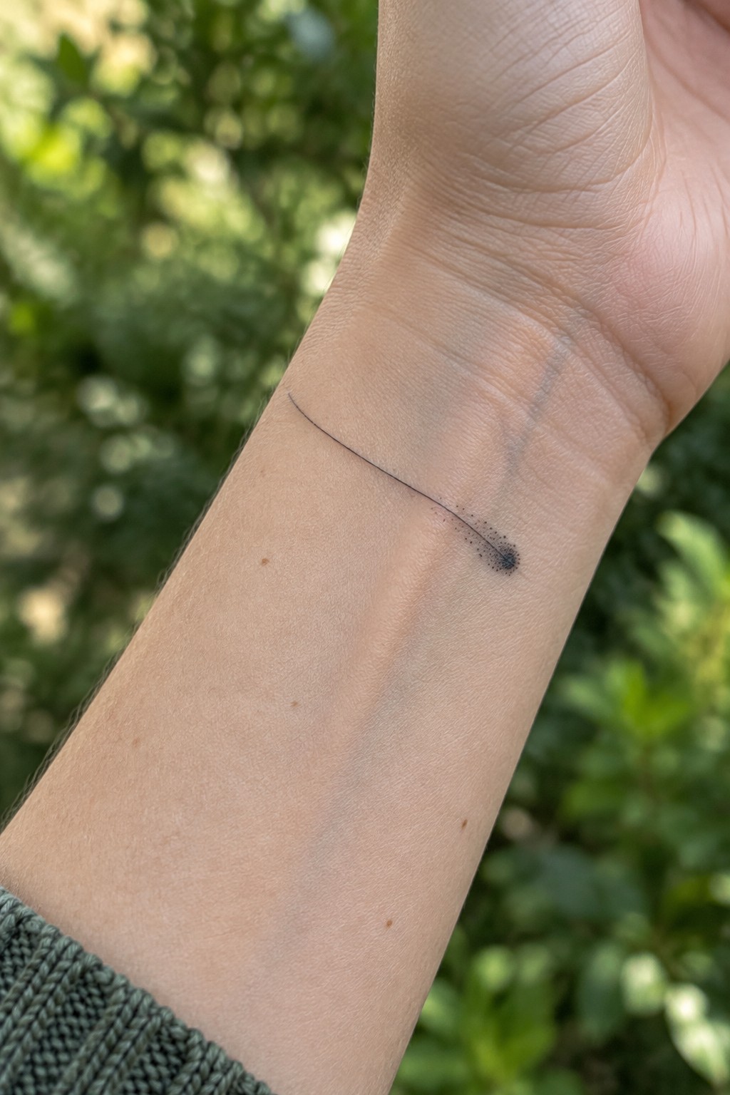 Fine line shooting star tattoo on the inner wrist with a thin tail and dotted comet head in single-needle style.