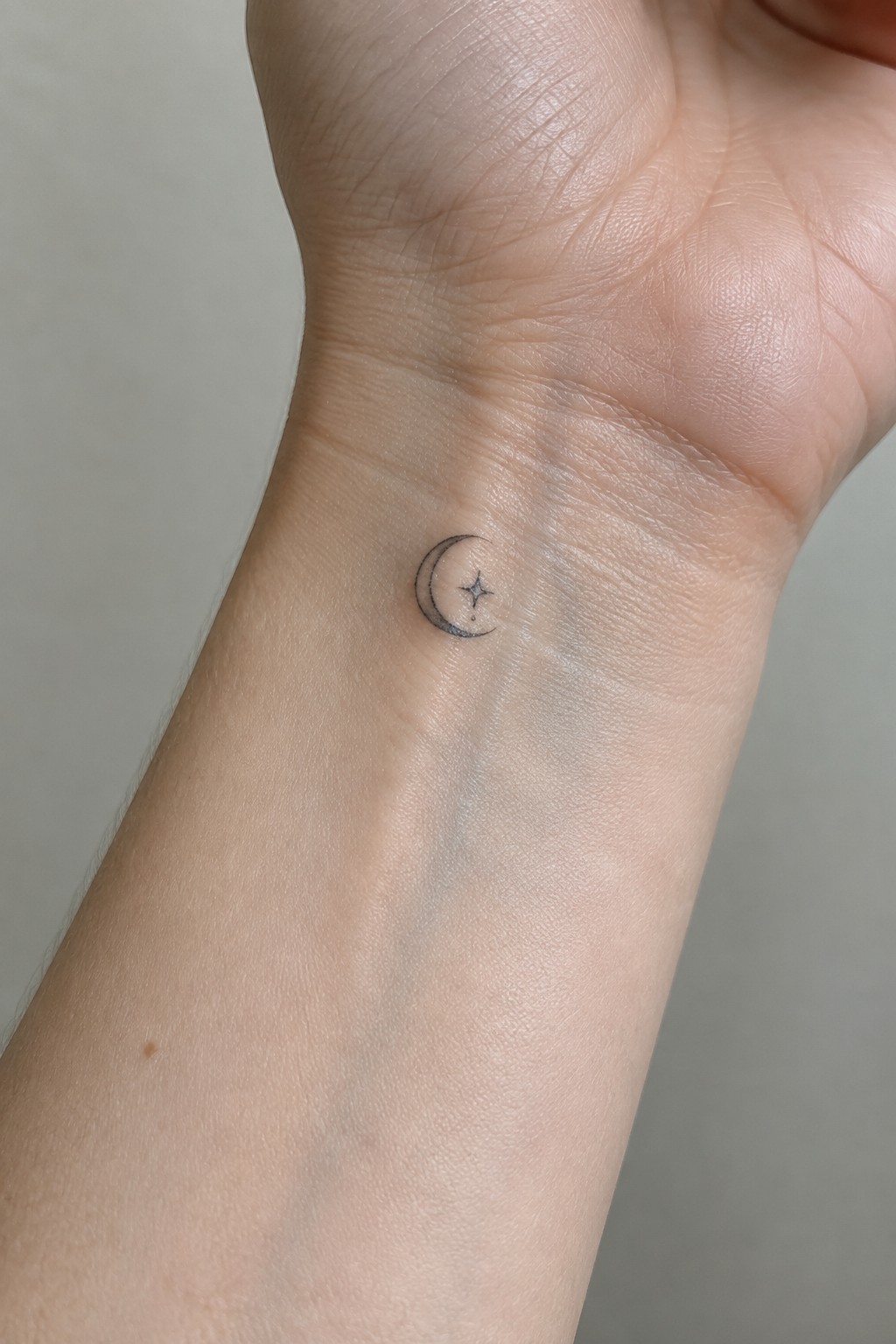 Small black crescent moon and star tattoo on light-skinned inner wrist