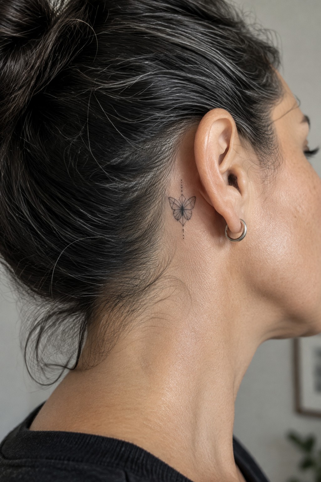 Small minimalist butterfly tattoo with dotted lines placed behind the ear on the side of the neck.