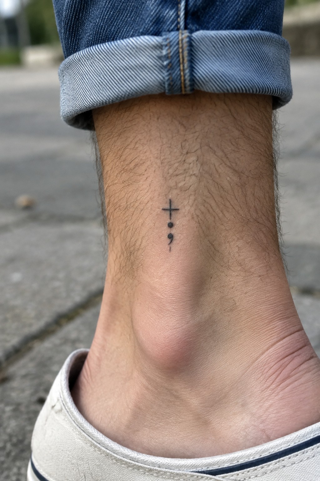 Cuffed blue jeans above white sneaker on ankle with cross and semicolon tattoo