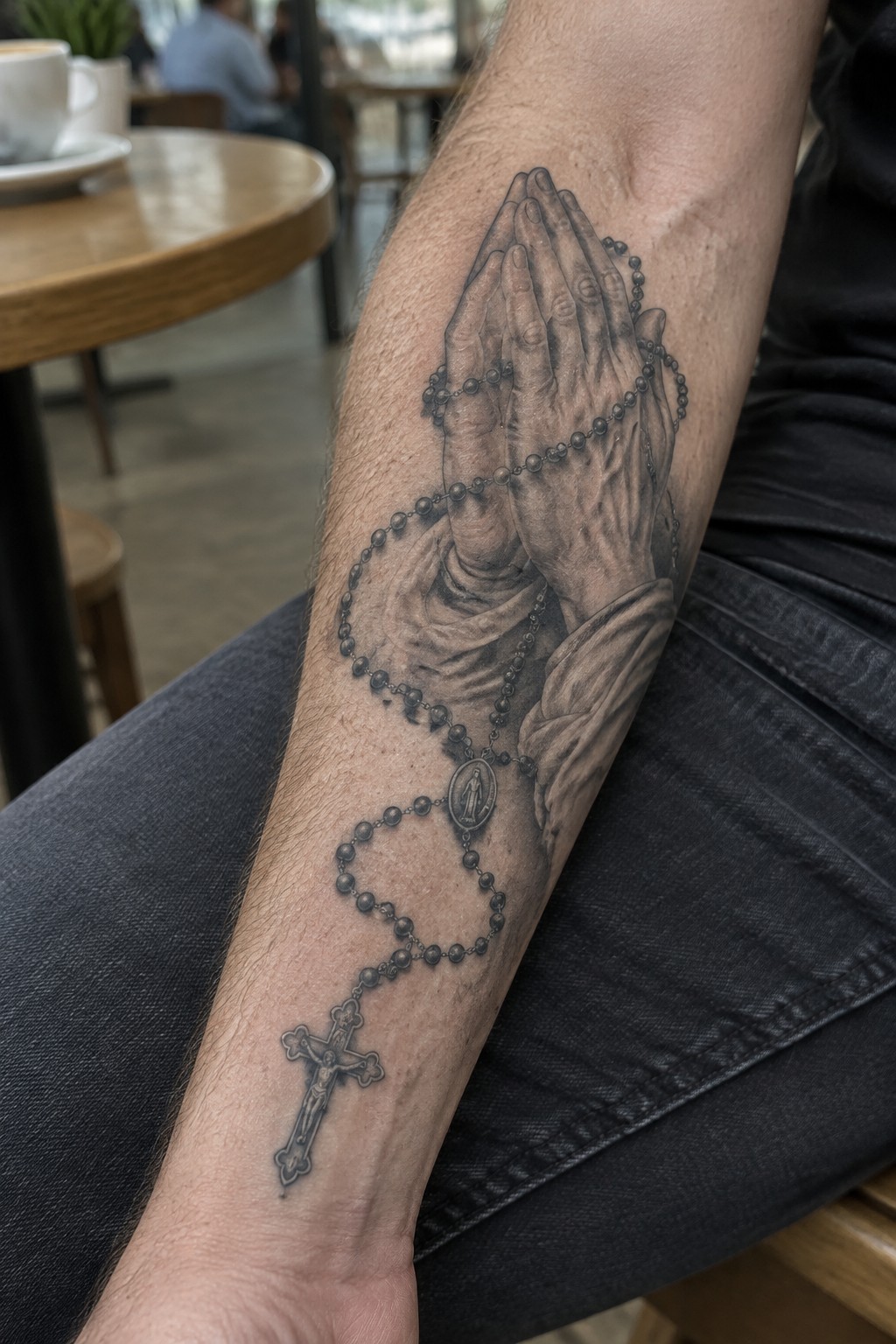 Black and gray praying hands rosary tattoo on forearm in jeans