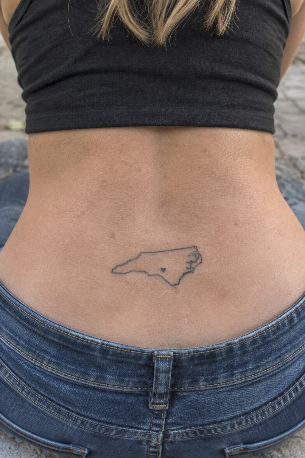 Lower back of person in black crop top and jeans with North Carolina tattoo.