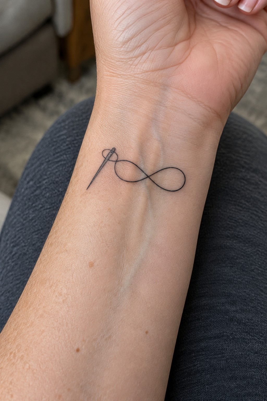 Fine line tattoo of a needle and infinity symbol on the inner wrist