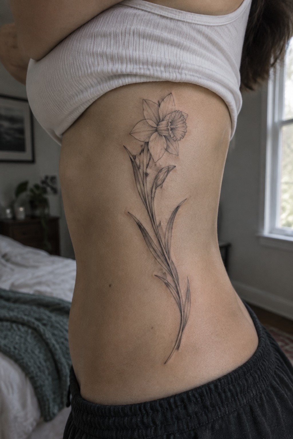 Daffodil tattoo with long stem on side torso below white crop top.