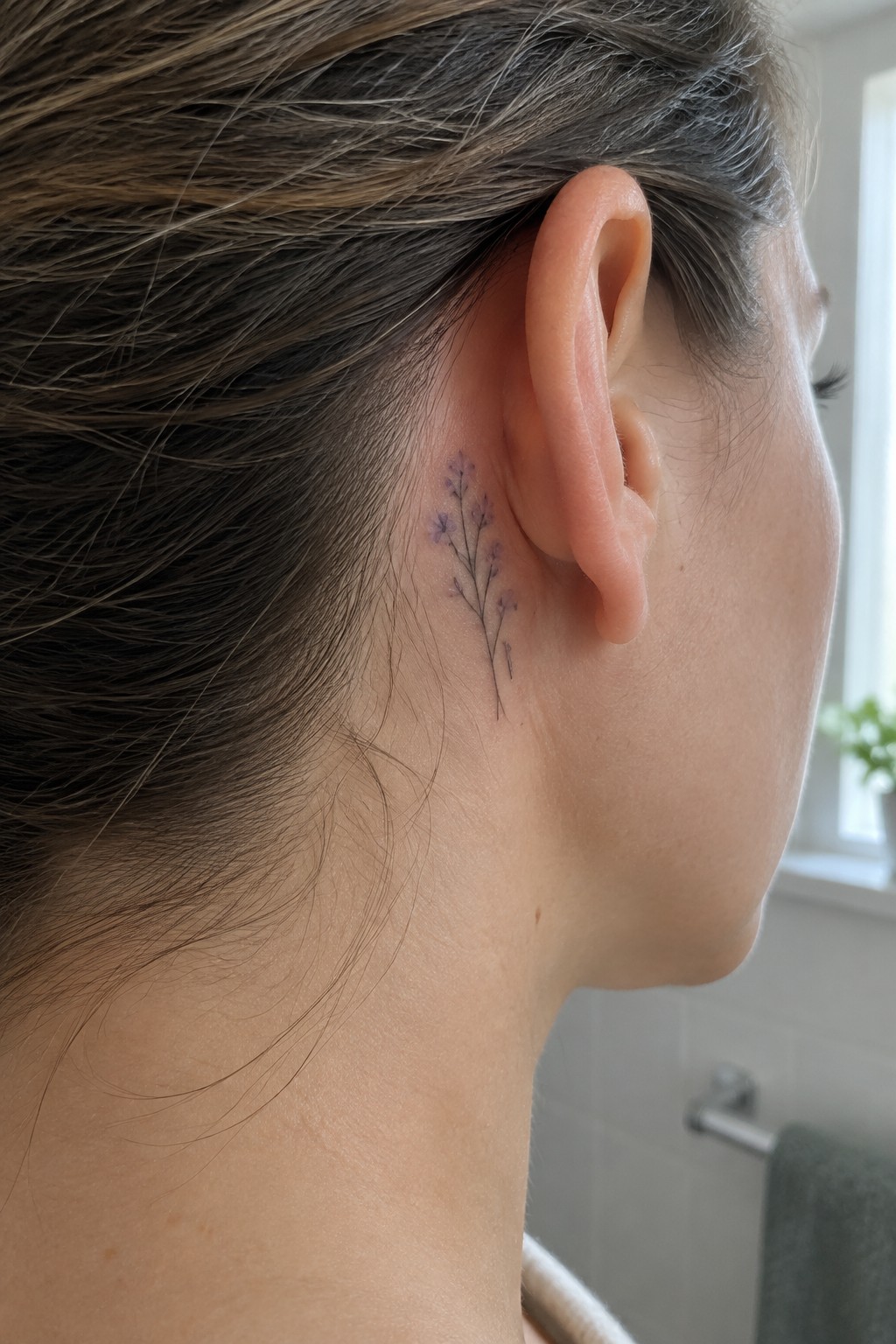 Fine line tattoo of small purple flowers placed behind the ear on a woman's head