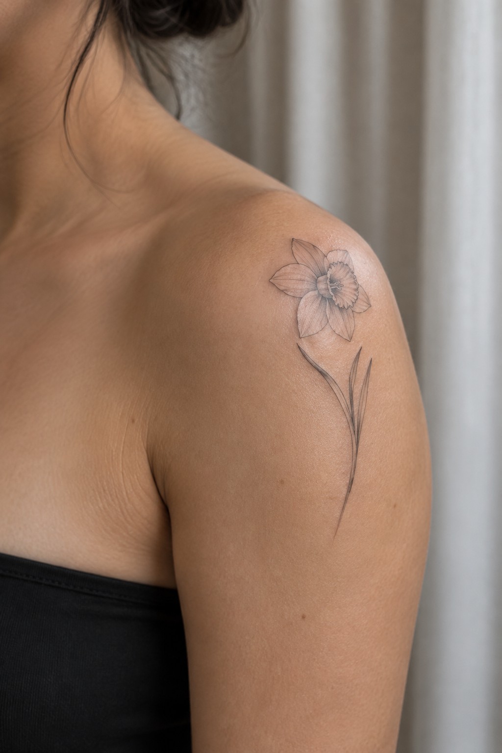 Daffodil tattoo on bare shoulder above black strapless top