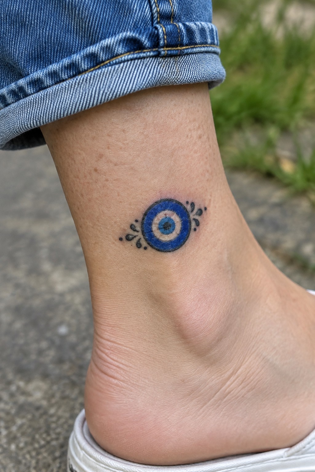 Cuffed blue jeans above ankle with blue evil eye tattoo and white shoe