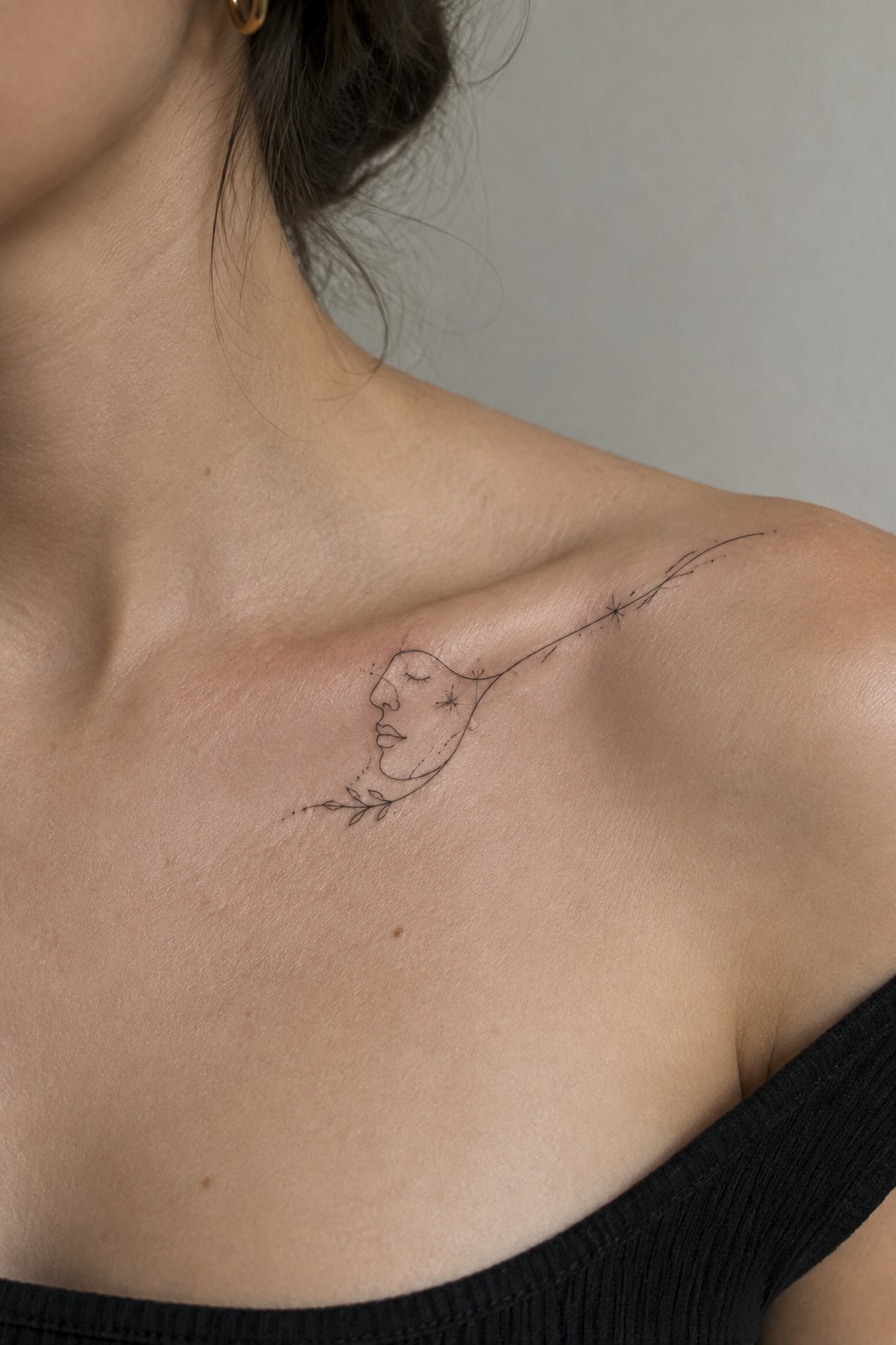 Delicate line tattoo of profile face with stars and leaves on bare shoulder above black top