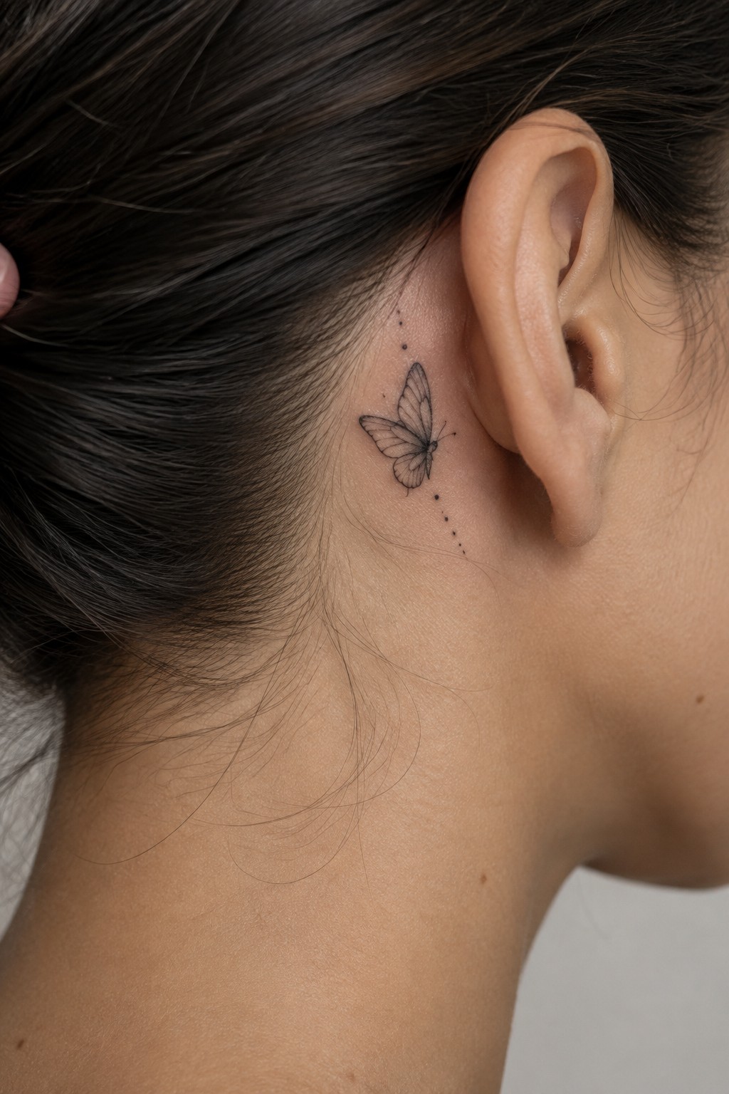 Dark hair pulled back showing butterfly tattoo with dotted trail behind ear