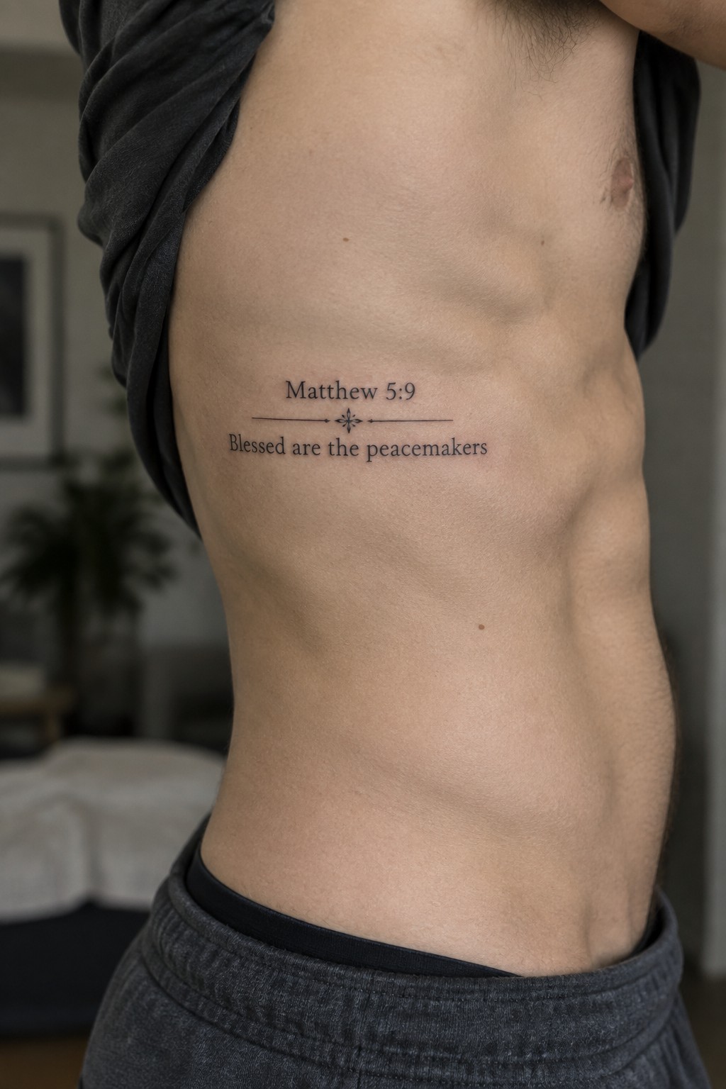 Man lifting gray shirt to show Matthew 5:9 peacemakers tattoo on ribs