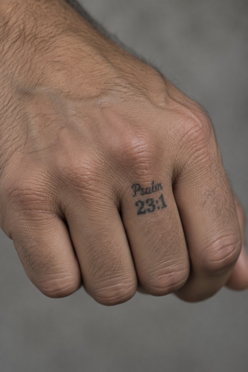 Clenched fist with Psalm 23:1 tattoo on wrinkled, hairy finger