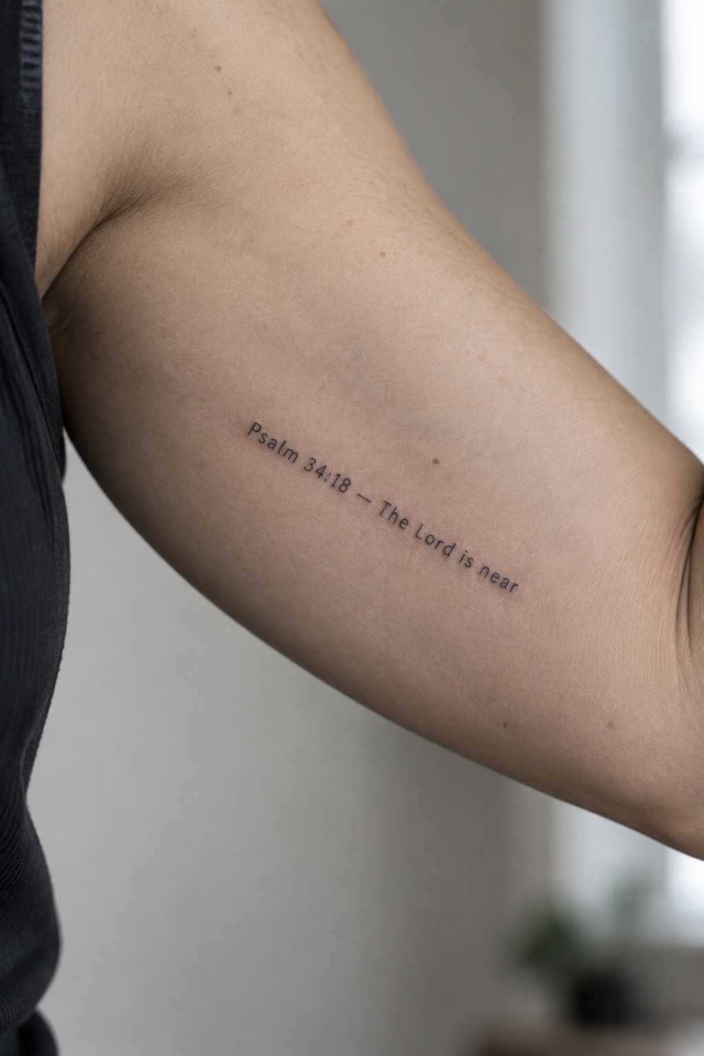 Small minimalist tattoo of Psalm 34:18 on the inner upper arm with the text The Lord is near in simple script.