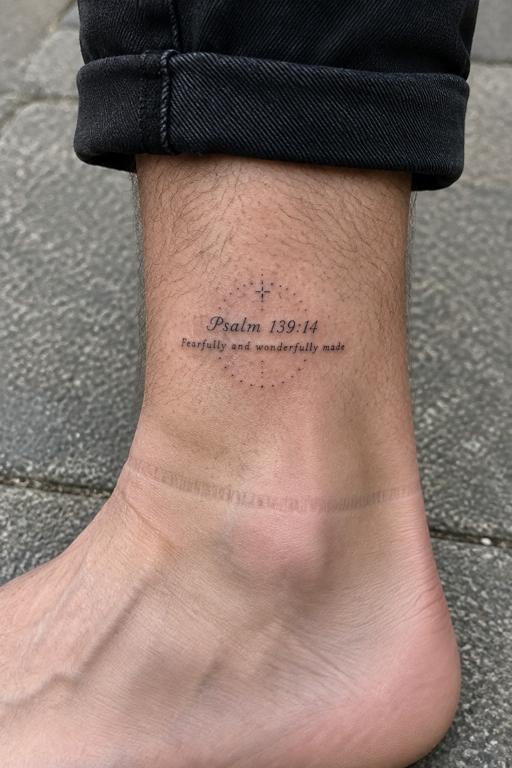 Black rolled-up jeans above Psalm 139:14 ankle tattoo with cross design and scar.