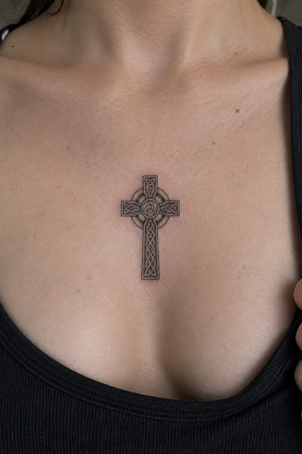 Detailed black Celtic cross tattoo with knots on upper chest above tank top