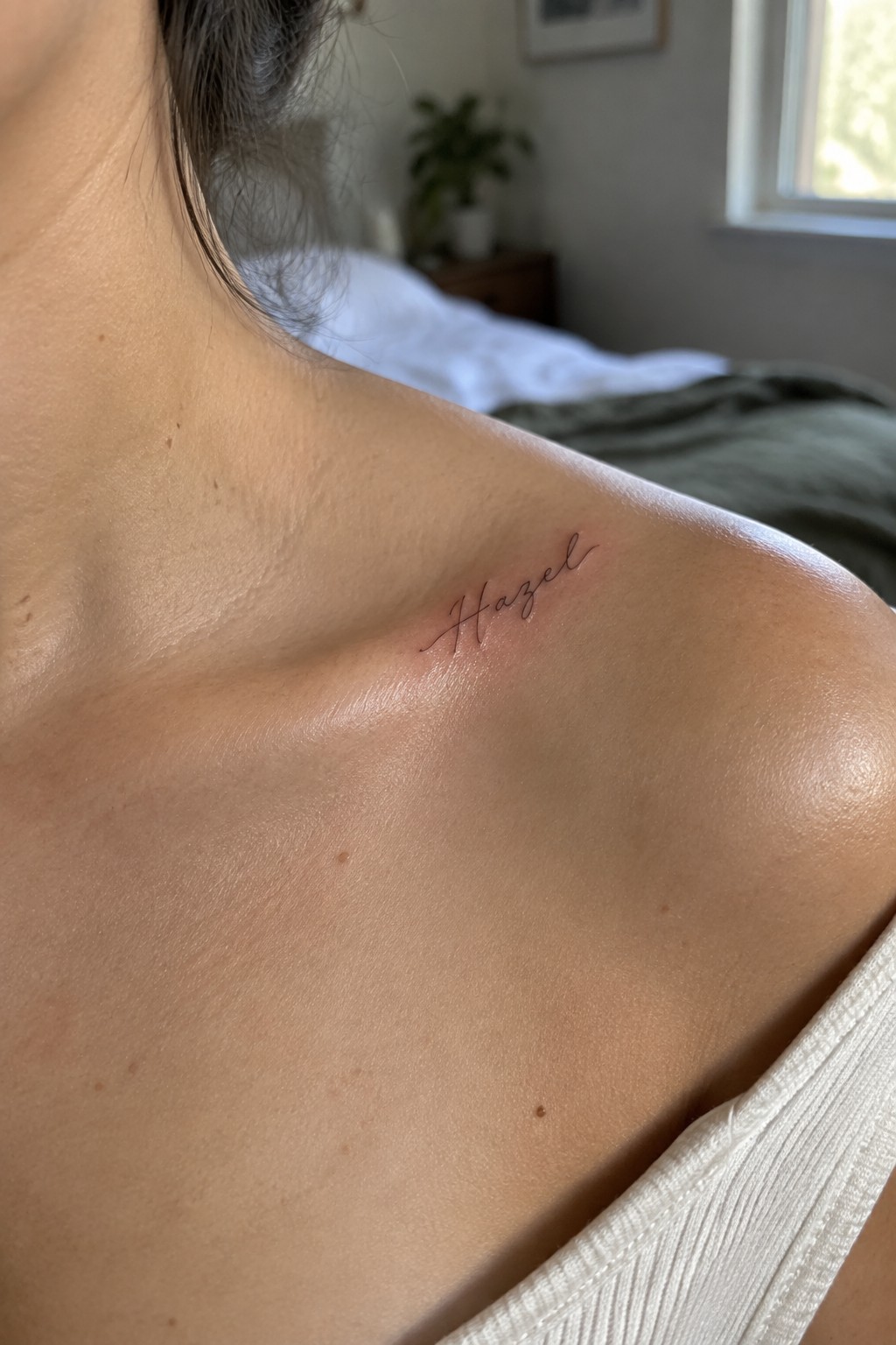 Fine line cursive tattoo of the name Hazel on a woman's collarbone area.