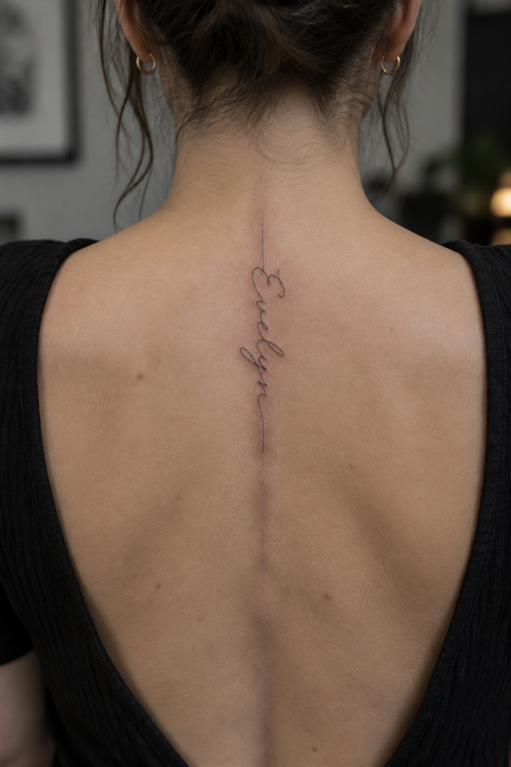 Woman's back with cursive Evelyn tattoo along spine, black low-back top.