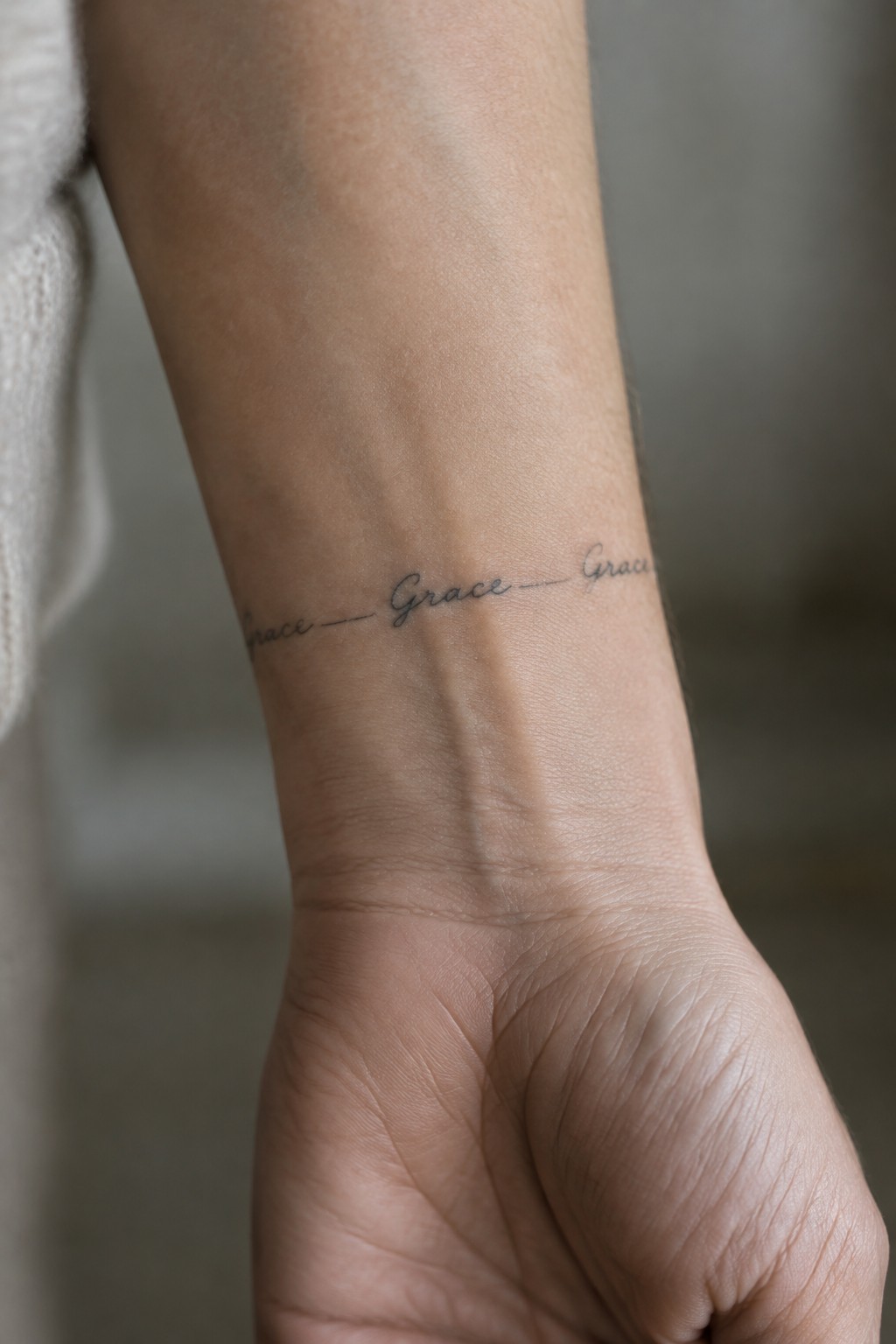 Close up of an inner wrist tattoo showing the name Grace written three times in connected handwritten fine line script