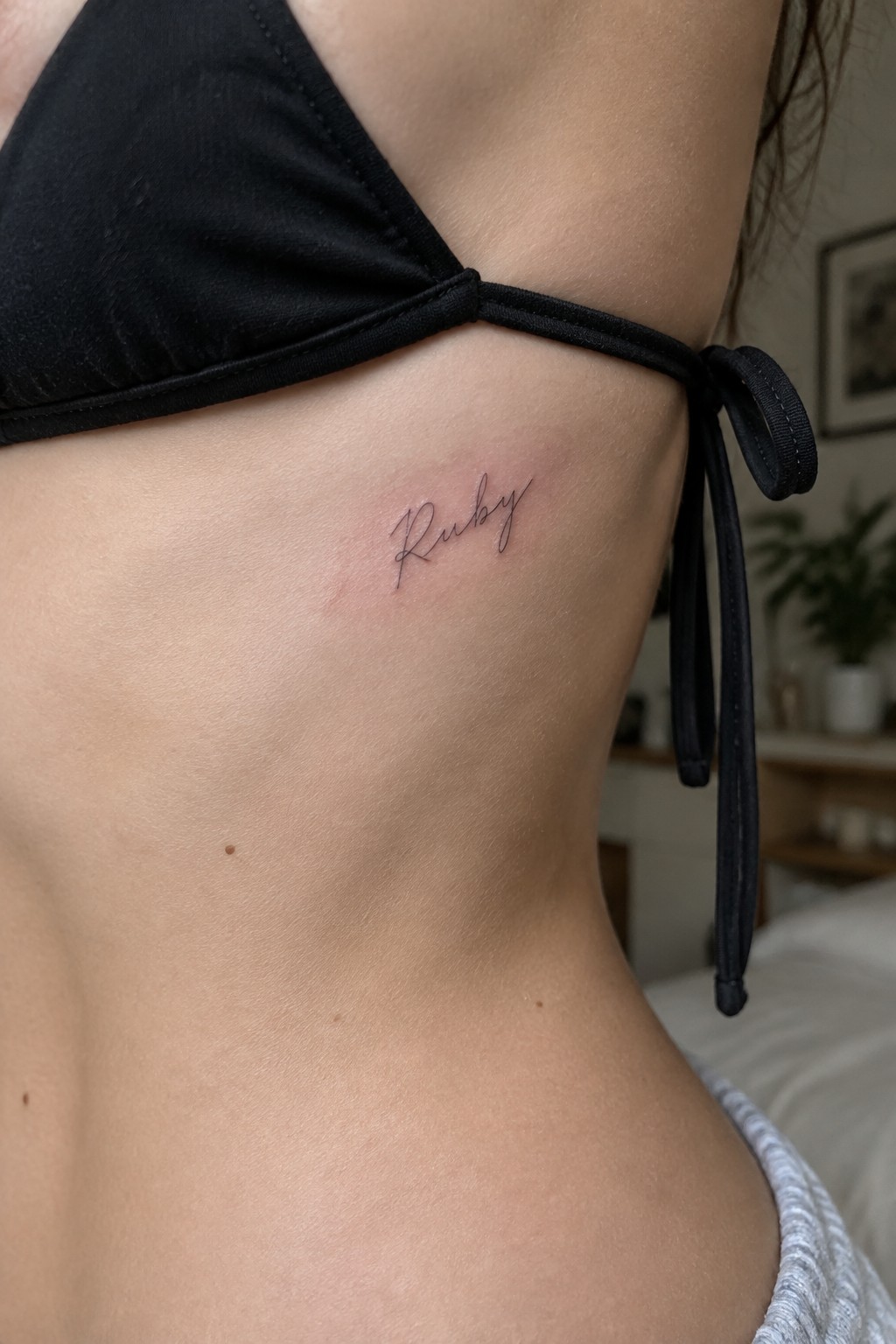 Black bikini top with cursive Ruby tattoo on ribcage skin