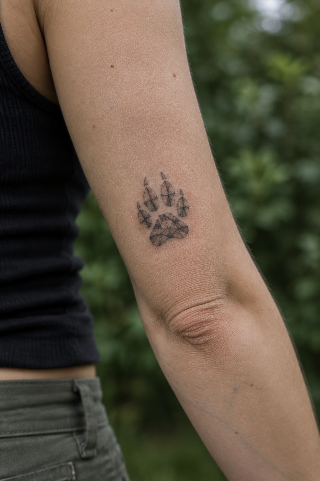 Geometric paw tattoo on upper arm with black tank top and blurred greenery