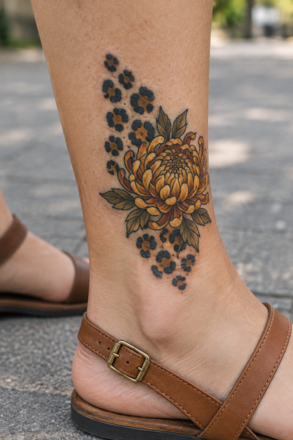 Yellow chrysanthemum tattoo with leopard spots on ankle above brown sandal