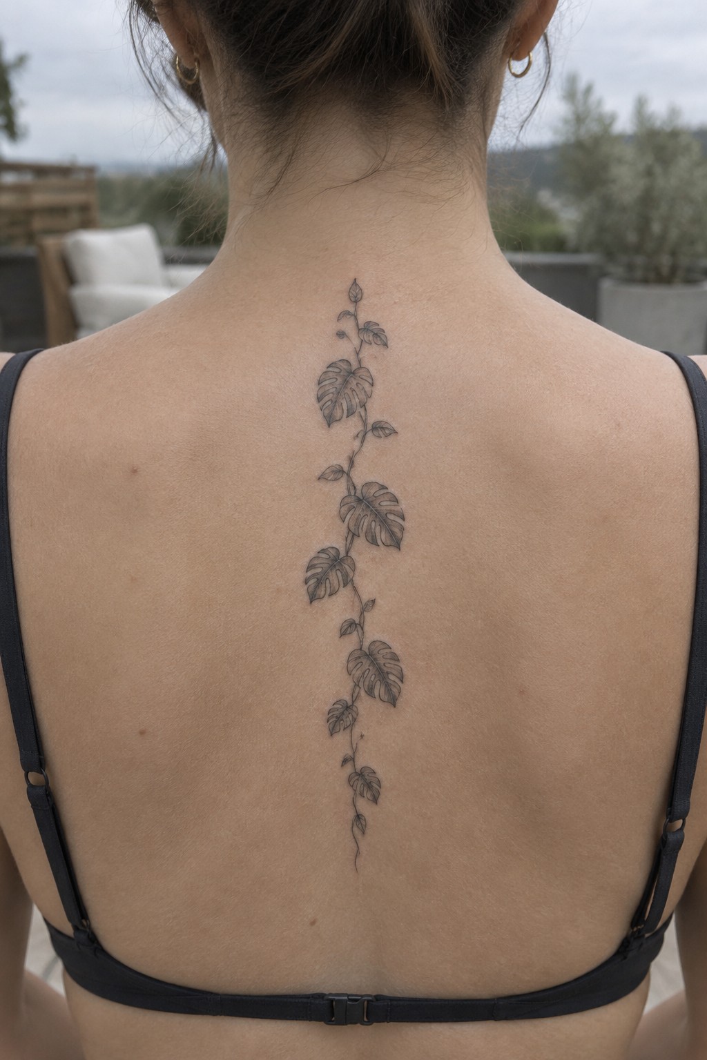 Woman's back with black leafy vine tattoo down spine wearing black bra