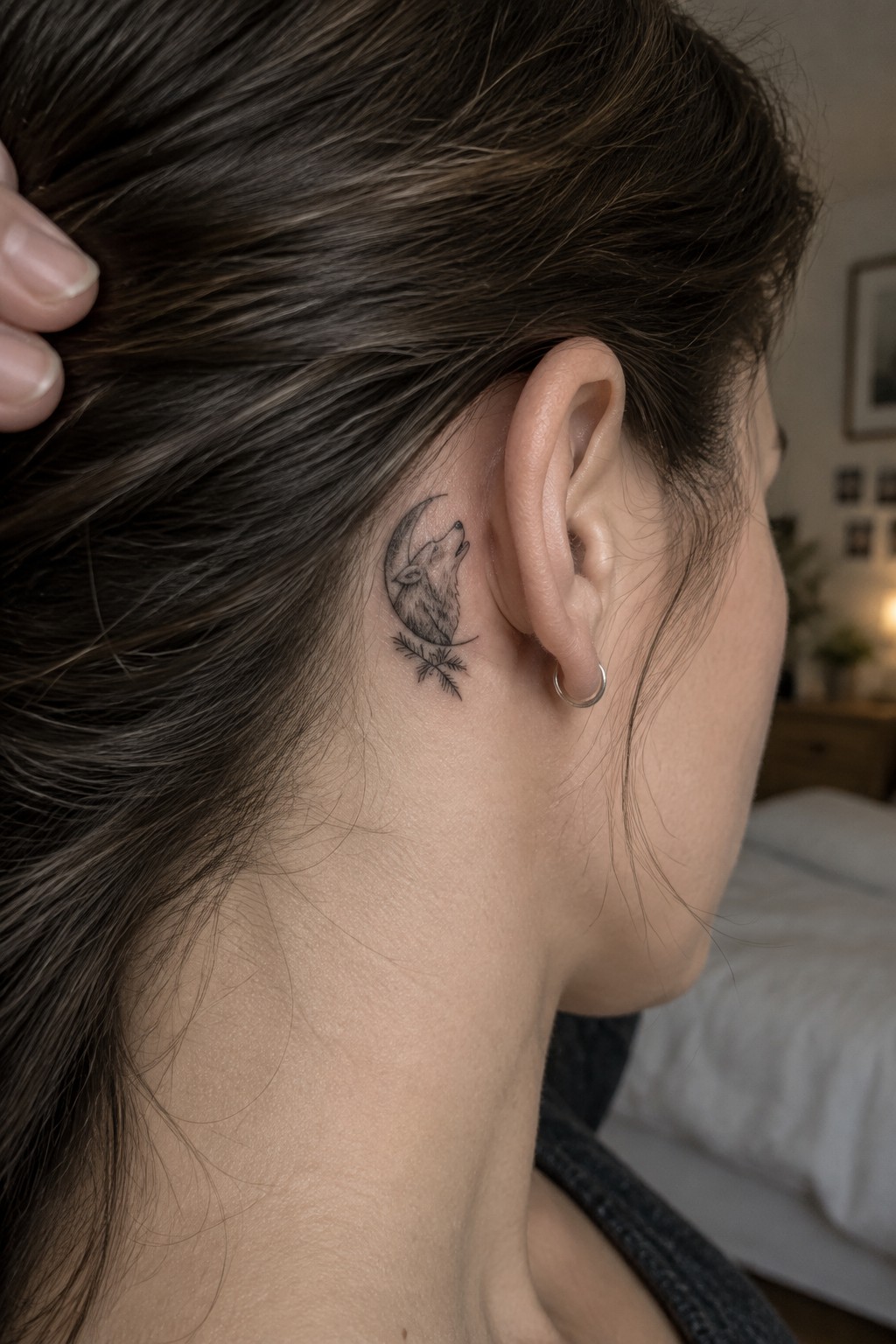 Wolf and moon tattoo behind woman's ear, brown hair held back.