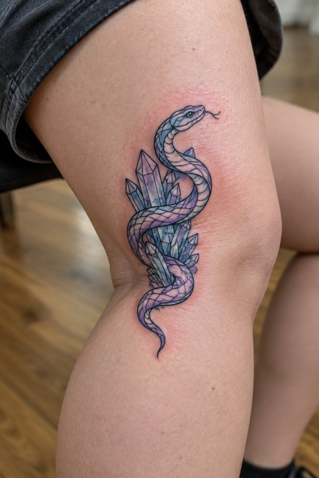Purple-blue snake coiled around crystals tattoo on person's thigh