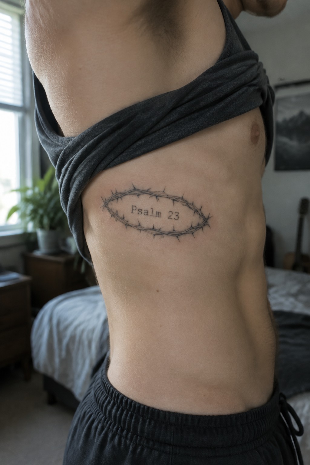 Shirt lifted to show thorny oval Psalm 23 tattoo on male torso
