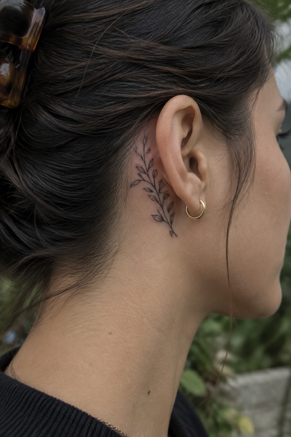 Dark-haired woman with leafy branch tattoo behind ear and gold hoop earring