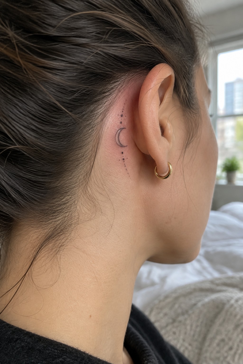 Woman's ear with gold hoop earring and crescent moon stars tattoo behind it