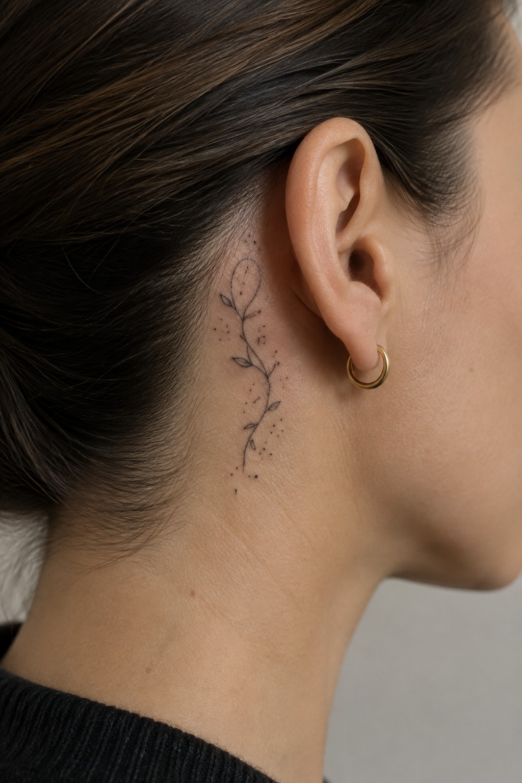 Delicate plant tattoo behind ear with gold hoop earring on neck