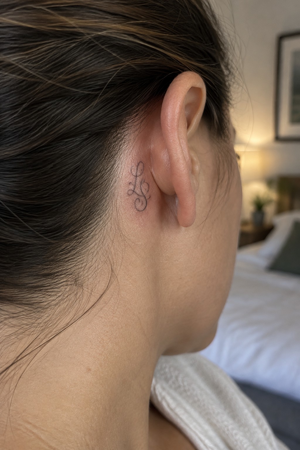 Small fine line monogram tattoo with cursive initials placed behind the ear.