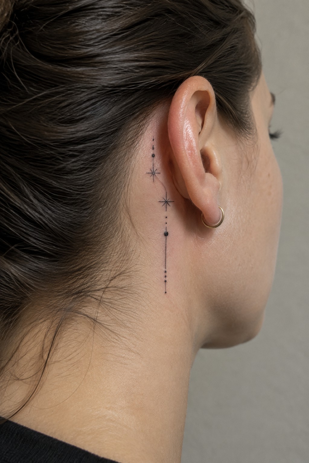 Star and dotted line tattoo behind ear with gold hoop earring.