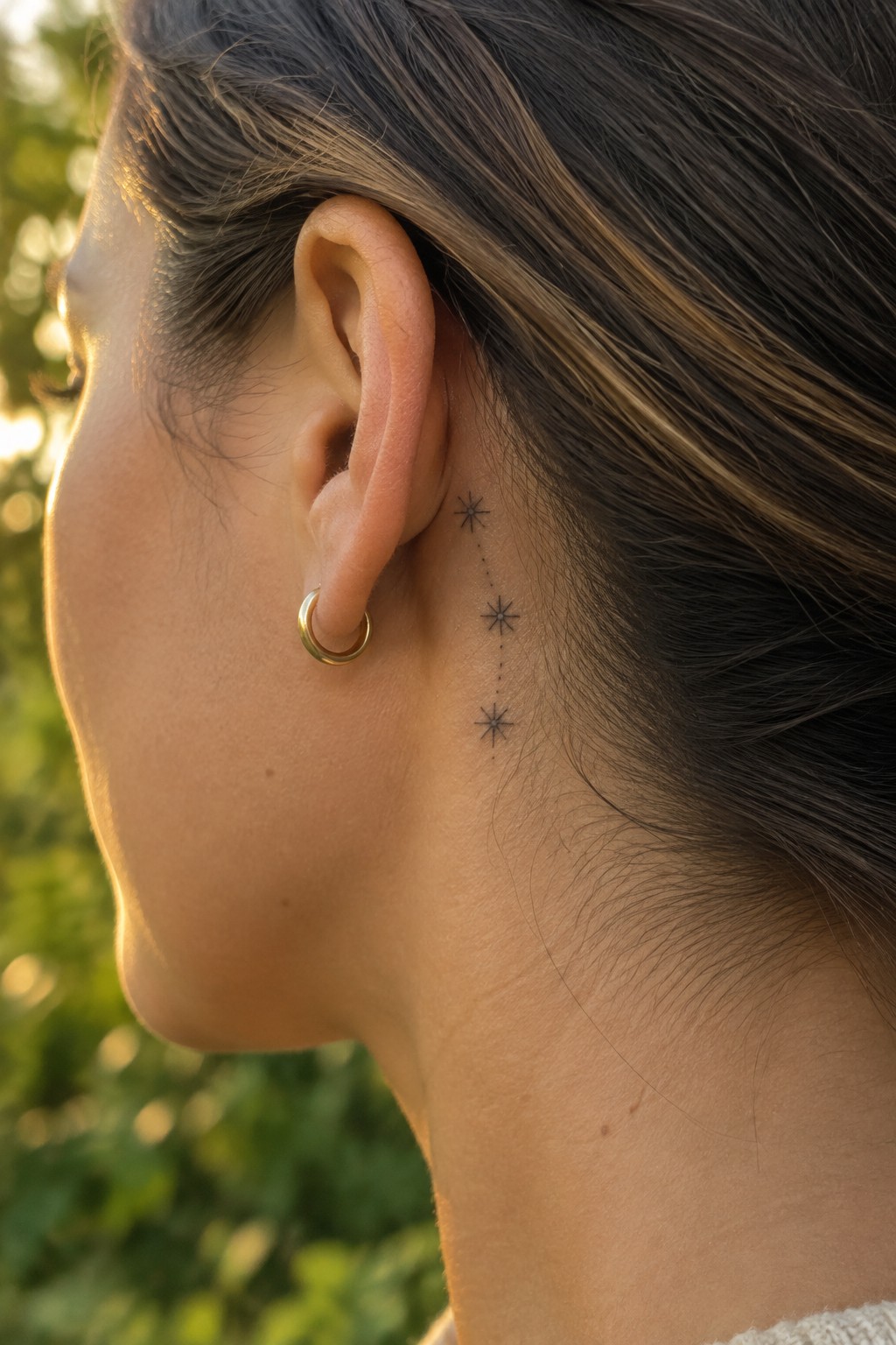 Woman's ear with gold hoop earring and vertical star constellation tattoo behind it