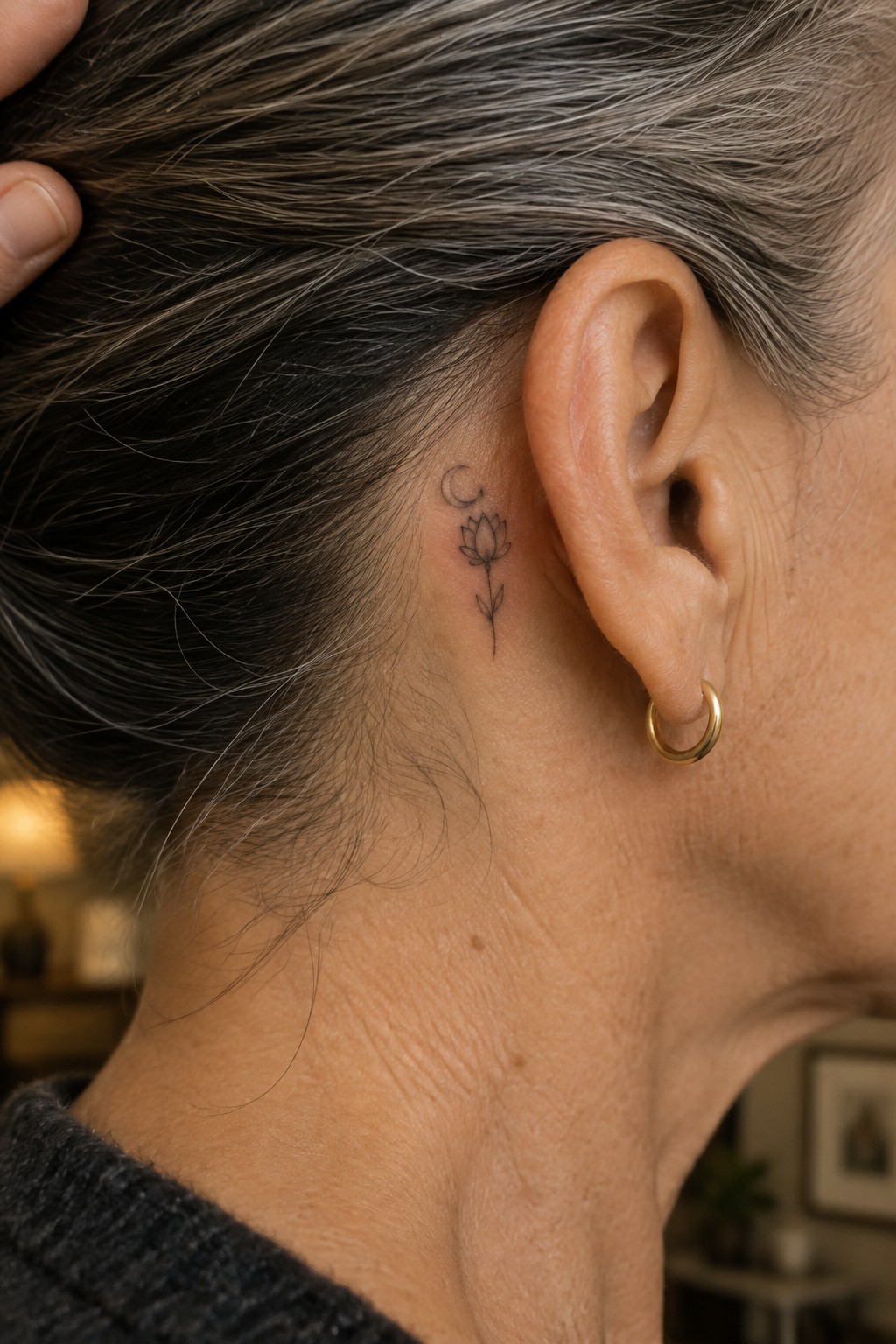 Fine line lotus flower with crescent moon tattoo placed behind a woman's ear on the side of the neck.