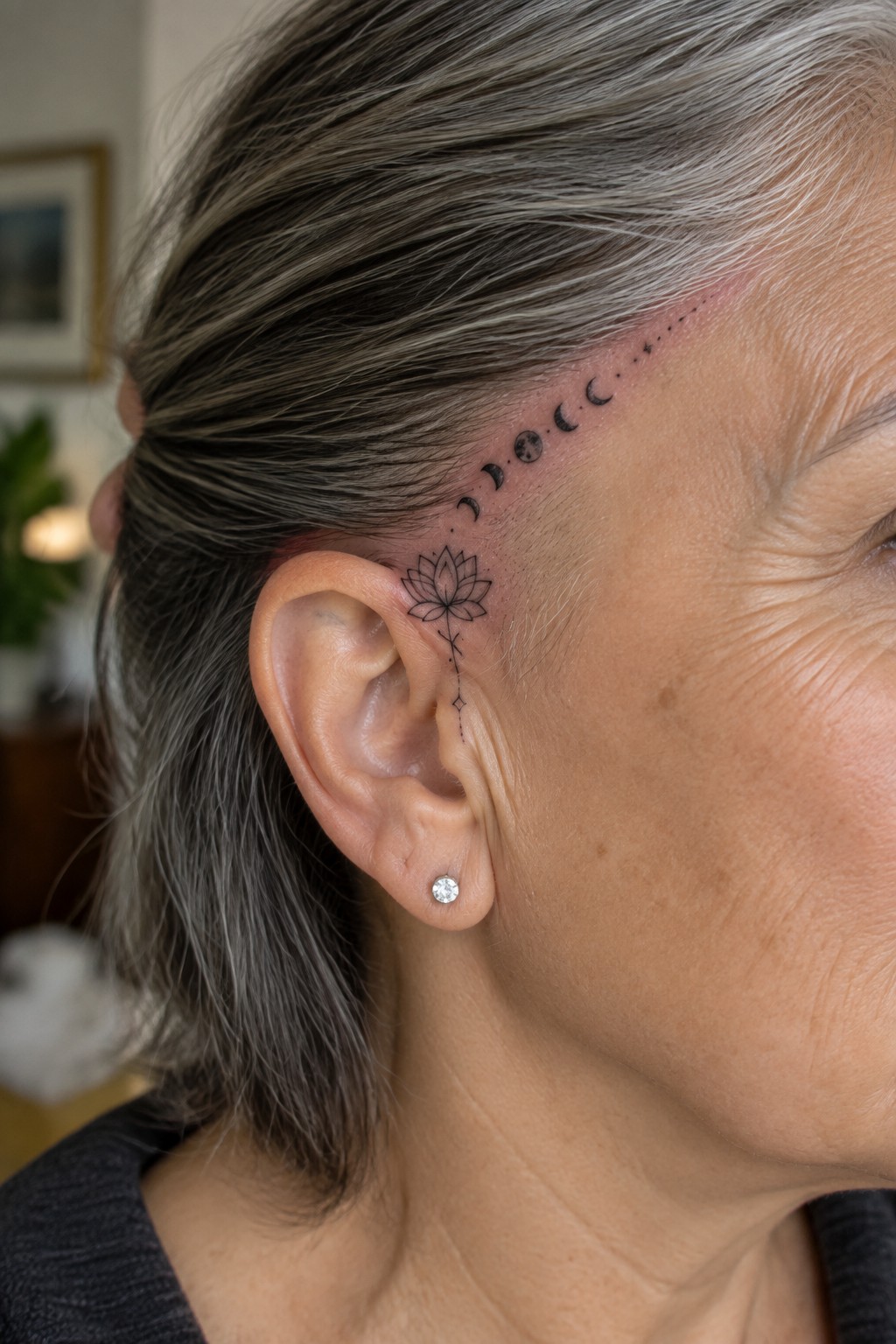 Gray-haired woman's ear with lotus flower and moon phases tattoo