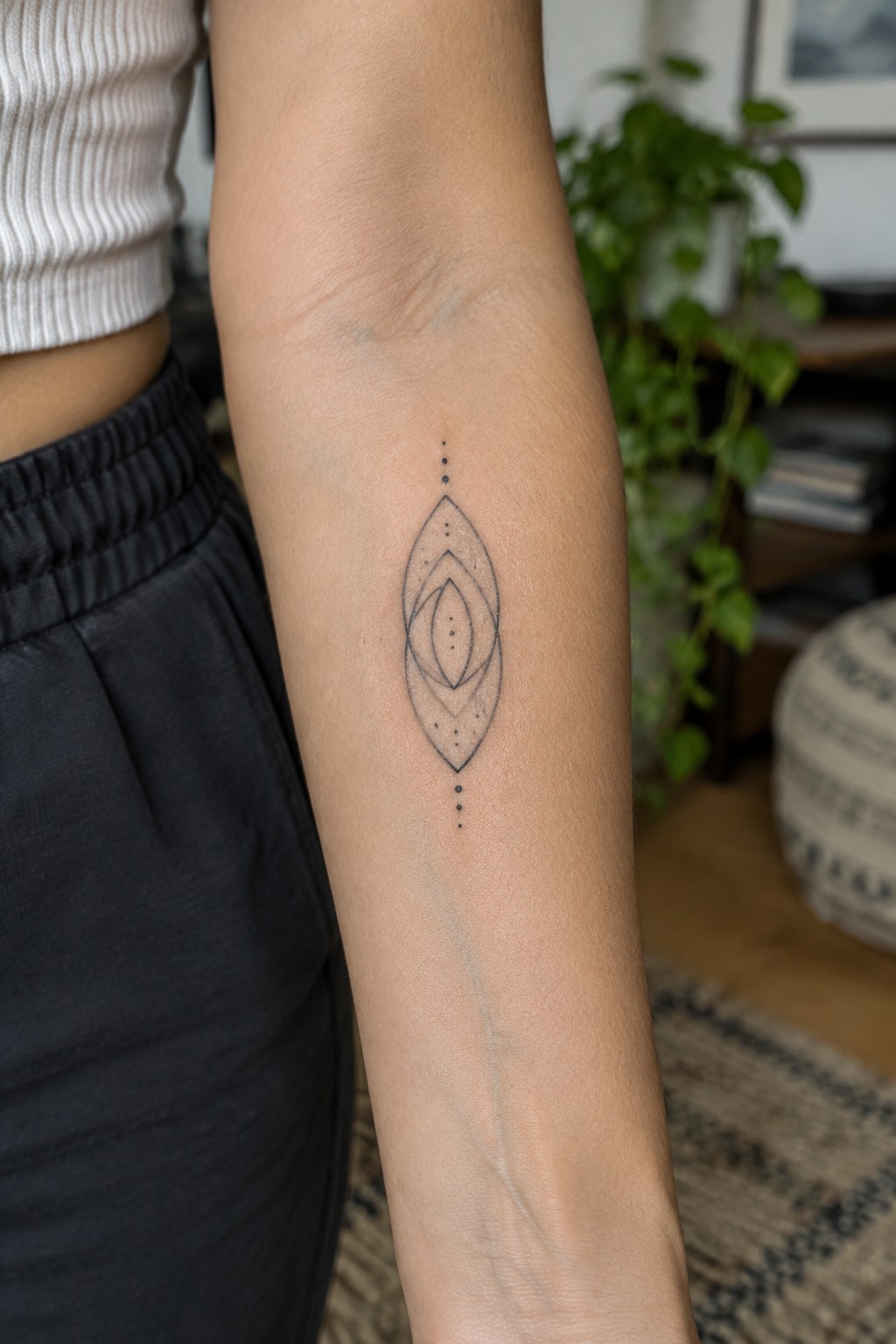Arm with minimalist geometric tattoo of ovals and dots, white top and black pants.