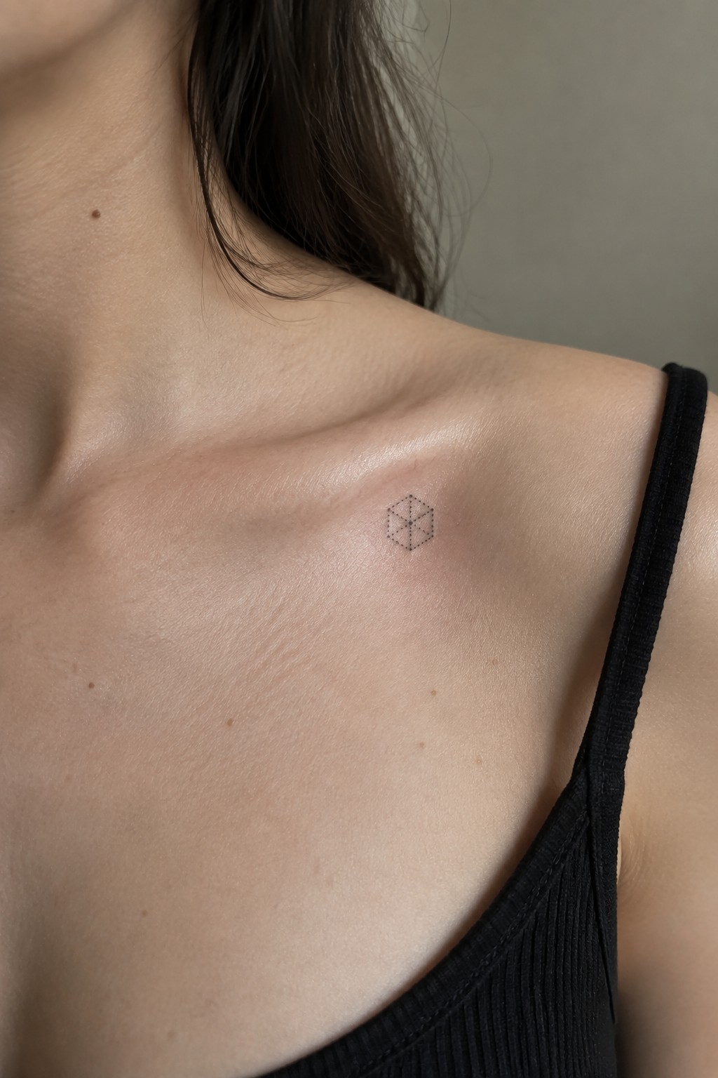 Close-up of shoulder with small geometric hexagon tattoo, black tank top strap visible
