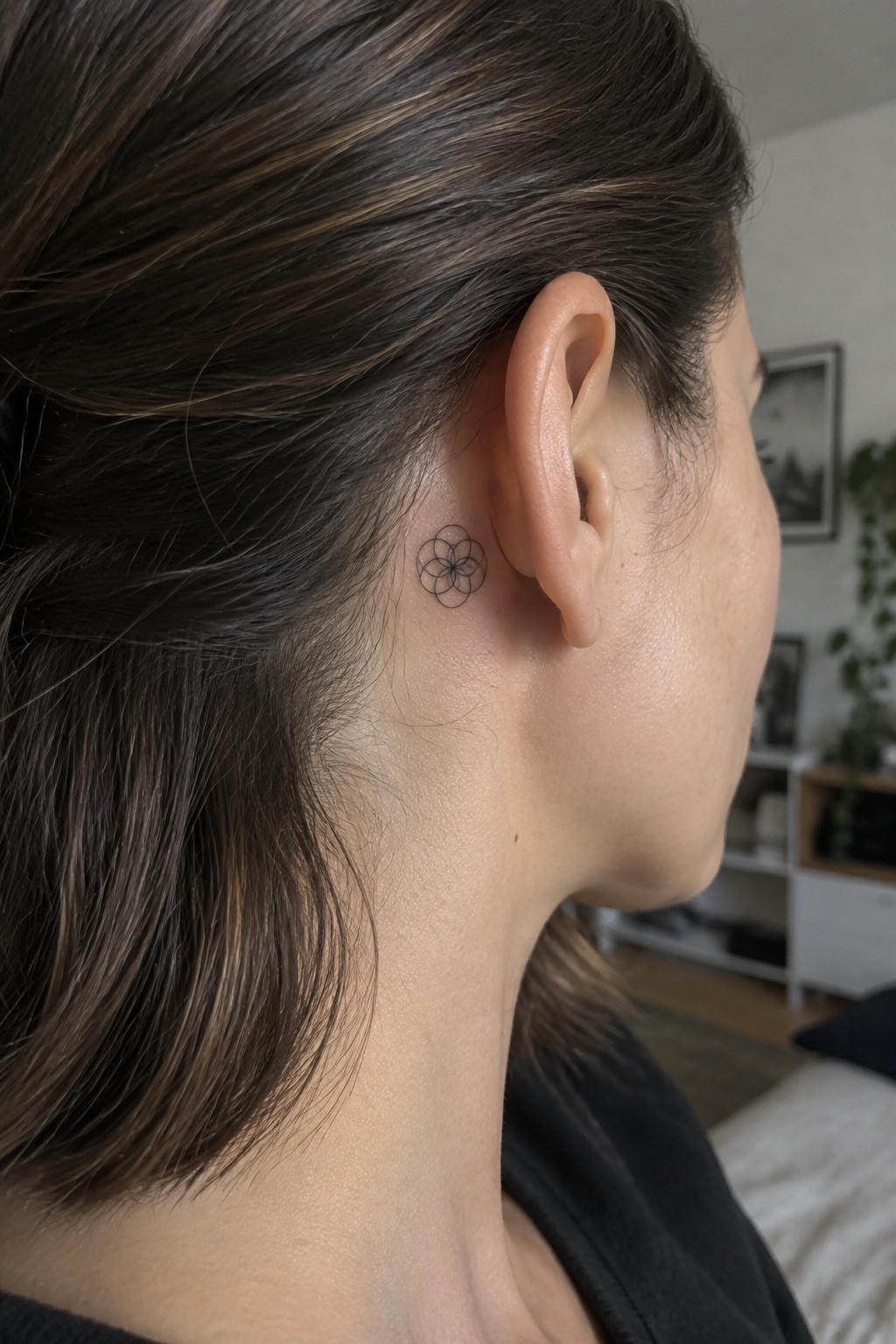 Woman's dark hair frames small black geometric flower tattoo behind her ear